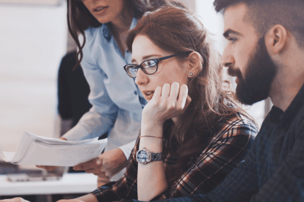 Three colleagues collaborating on a laptop in an office, focused on a digital marketing project